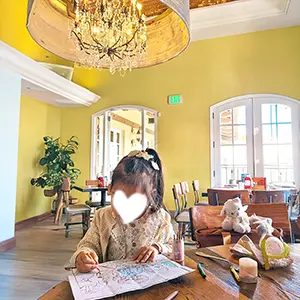 Child coloring Bob Ross coloring paper under a grand chandelier