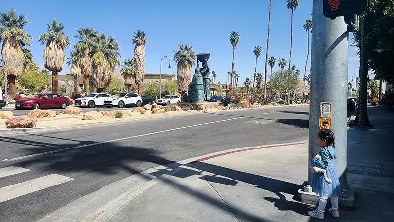 Ellie pressing the "Wait" button at the crosswalk in front of Agua Caliente Cultural Plaza