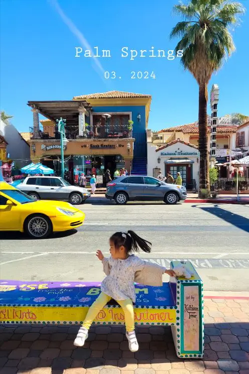 Child resting on a bench under the shade of palm trees in colorful downtown Palm Springs