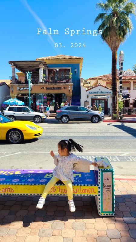 Child resting on a bench under the shade of palm trees in colorful downtown Palm Springs